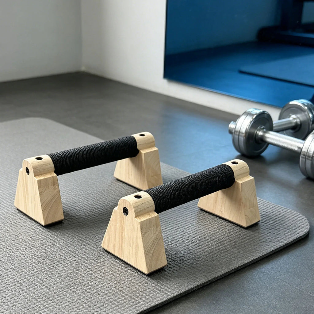 Wooden parallettes set with black grip handles and arched base standing on floor mat