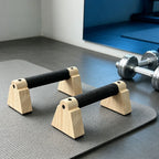 Wooden parallettes set with black grip handles and arched base standing on floor mat